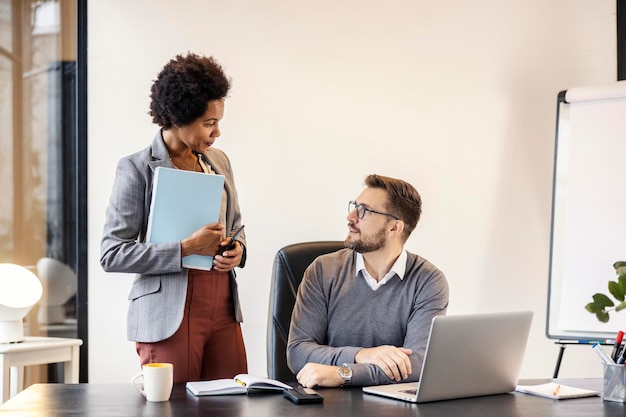 Un directeur est assis au bureau pendant qu'une femme d'affaires afro-américaine fait un rapport.