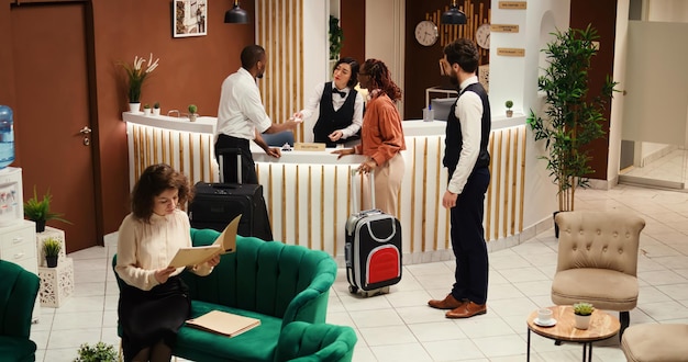 Directeur d'hôtel concentré vérifiant les documents de réservation des touristes pendant qu'ils sont assistés par le personnel de la conciergerie. Bellboy aidant les clients avec leurs bagages après l'enregistrement.