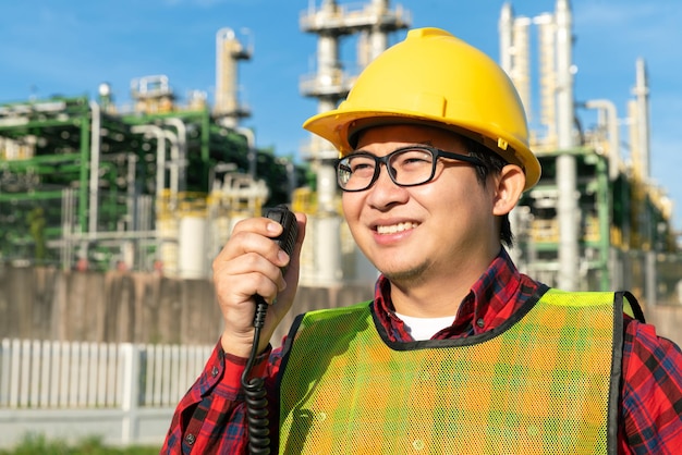 Le directeur de l'ingénieur porte un uniforme de casque de sécurité parle avec l'équipe d'ingénieurs avec un talkie-walkie radio pendant le travail avec le pétrole pétrochimique de raffinerie dans le contexte des affaires d'une usine chimique