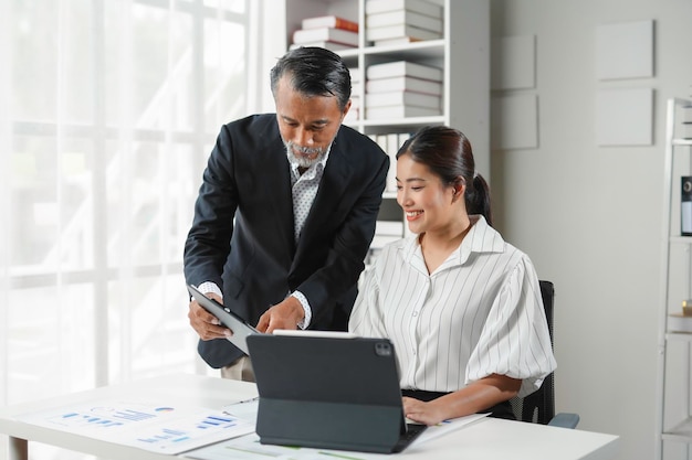 Un directeur principal démontre du contenu sur une tablette numérique à une jeune femme d'affaires asiatique dans le bureau
