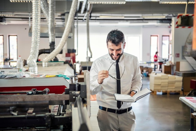 Un directeur tenant l'agenda entre ses mains et vérifiant la machine d'impression dans l'imprimerie