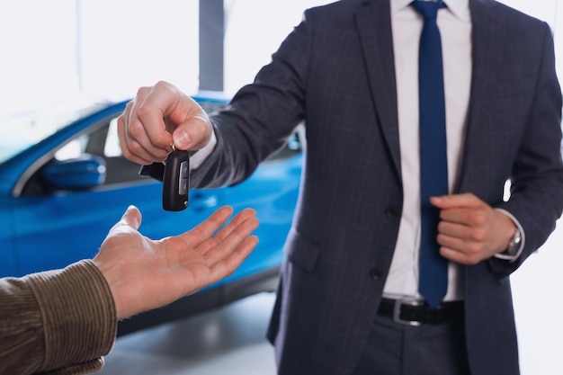 Un directeur des ventes en costume passe la clé de la voiture à l'acheteur dans le contexte de la voiture achetée