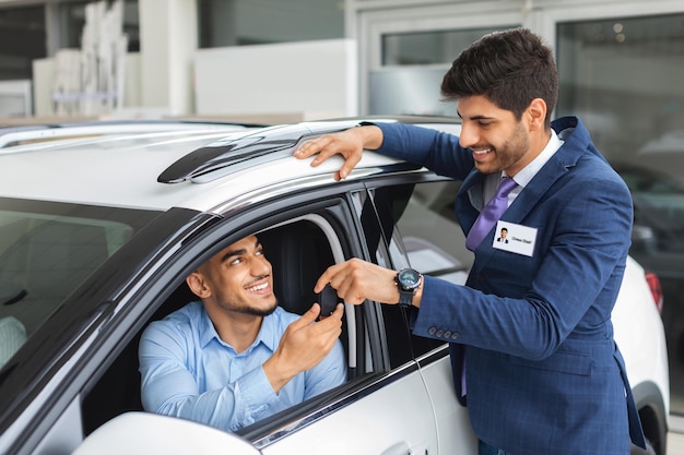 Directeur des ventes joyeux donnant la clé de la voiture au propriétaire