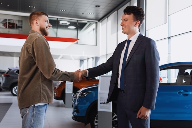 Un directeur des ventes serre la main d'un client masculin sur le fond d'un concessionnaire automobile Heureux nouvel acheteur de voiture