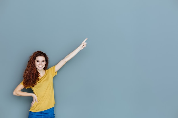 Cette direction. Heureuse femme agréable ravie souriant et pointant avec sa main tout en vous regardant