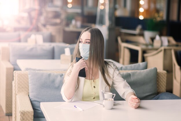 Une directrice en costume et masque médical travaille à distance dans un café de la rue.