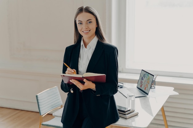 Directrice féminine tenant un cahier et un crayon tout en s'appuyant sur le bureau