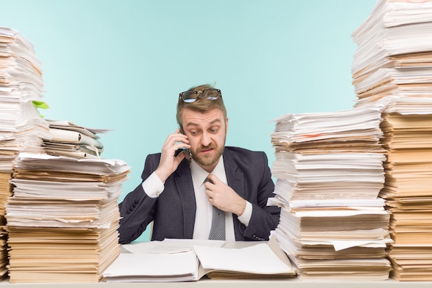 Un dirigeant d'entreprise au bureau et des tas de paperasse, grondé au téléphone pour un travail mal fait -