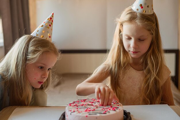 Dirigez les enfants filles casquettes sans hésitation manger un beau gâteau d'anniversaire avec leurs mains à la maison l'anniversaire des enfants pendant l'isolement de la quarantaine de la maladie