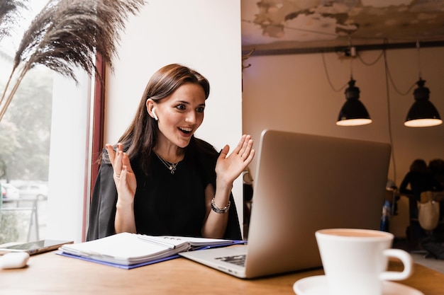 Discussion d'équipe et résolution de problèmes à distance Une fille responsable avec un ordinateur portable gesticule discute des tendances et des tâches au café Réunion vidéo en ligne avec des collègues et des partenaires commerciaux