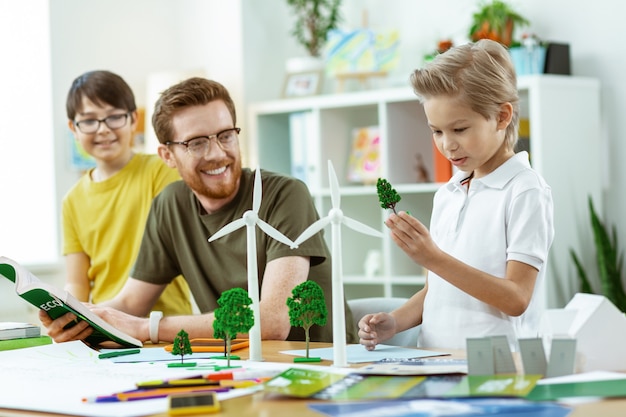 Discuter d'écologie. Jeune étudiant curieux portant un exemple en plastique d'un arbre et l'inspectant attentivement