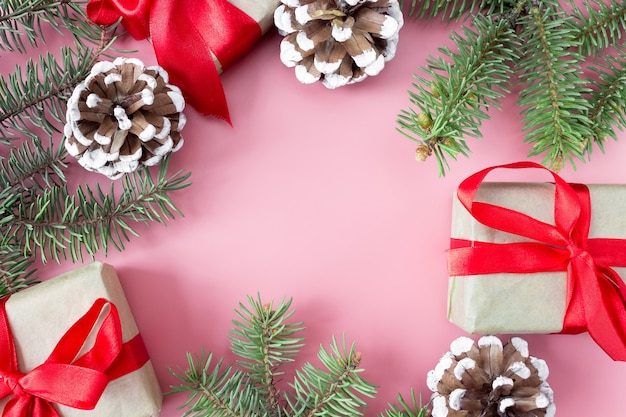 Disposition de Noël et du nouvel an sur fond rose, un cadre de branches d'épinette, de cônes et de coffrets cadeaux.