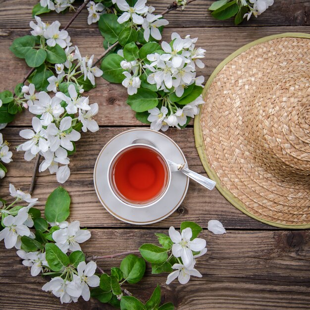 Disposition de printemps avec des branches d'un pommier en fleurs, une tasse de thé et un chapeau de paille