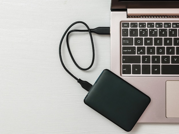 Disque Dur Externe Connecté à Un Ordinateur Portable Sur Un Bureau Léger. La Vue Du Haut. Le Concept De Stockage De Sauvegarde. Mise à Plat.