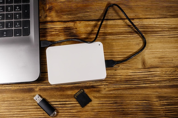 Disque dur externe connecté à un ordinateur portable Carte mémoire SD et lecteur flash USB sur un bureau en bois Vue de dessus Concept de stockage de données