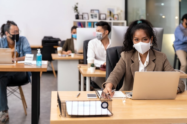 La distance sociale au bureau avec une équipe commerciale portant des masques faciaux