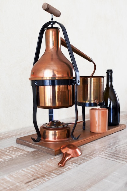 Un distillateur en cuivre avec une bouteille de vin sur une table.