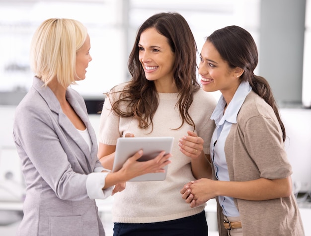 Dites-moi ce que vous en pensez... Photo recadrée de trois femmes d'affaires regardant une tablette au bureau.