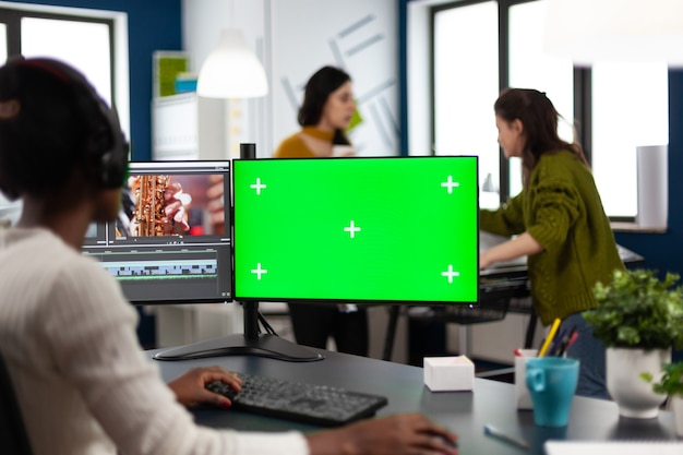 Éditeur vidéo de femme africaine avec des écouteurs traitant le montage de film travaillant à l'écran vert