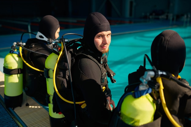 Divemaster et deux plongeurs en équipement de plongée se préparant à la plongée, école de plongée. Enseigner aux gens à nager sous l'eau, intérieur de la piscine intérieure sur fond