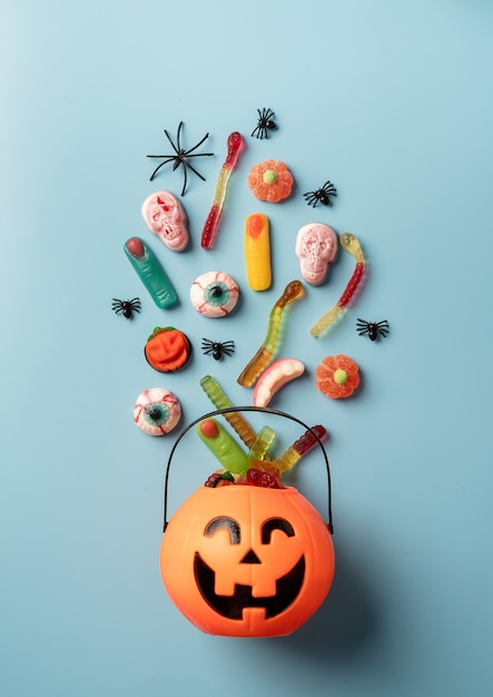 Divers bonbons et bonbons d'halloween dans un pot de citrouille sur fond bleu uni