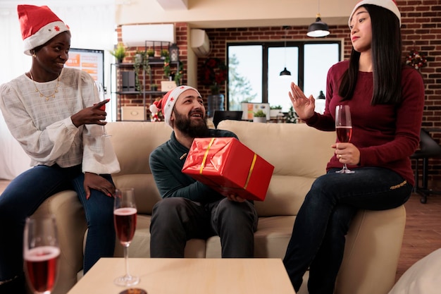 Divers collègues échangeant des cadeaux à la fête de noël dans un bureau festif décoré d'ornements de noël. Des gens heureux qui donnent une boîte cadeau pour célébrer la fête des vacances d'hiver avec des décorations.