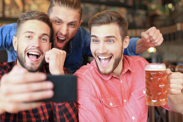 Divers fans de football regardent le football sur smartphone et célèbrent le score de la victoire au pub.