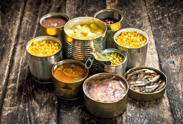 Divers légumes en conserve, viande, poisson et fruits dans des boîtes de conserve sur table en bois.