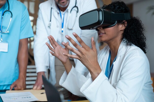 Photo divers médecins, hommes et femmes, portant des masques, assis à table et utilisant des lunettes vr