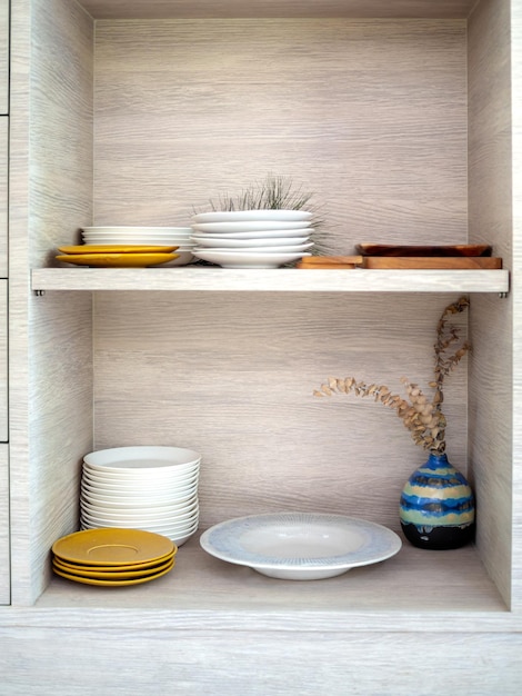 Divers plats en céramique blancs et jaunes ordonnés dans une armoire en bois