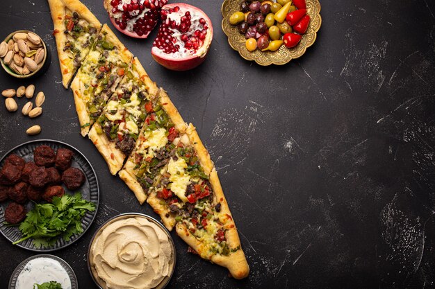 Divers plats turcs : pizza pide, kebab de viande avec salade de taboulé, falafel, houmous, olives et meze du Moyen-Orient sur une vue de dessus de table noire avec espace de copie. Cuisine arabe ethnique, cuisine de la Turquie