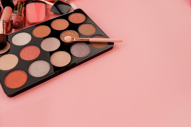 Divers produits de maquillage sur fond rose avec fond.