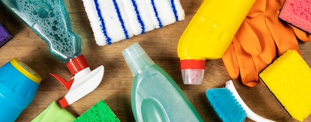 Divers produits de nettoyage, sprays, bouteilles, éponge, gants en caoutchouc sur fond bois, vue de dessus. Concept de nettoyage