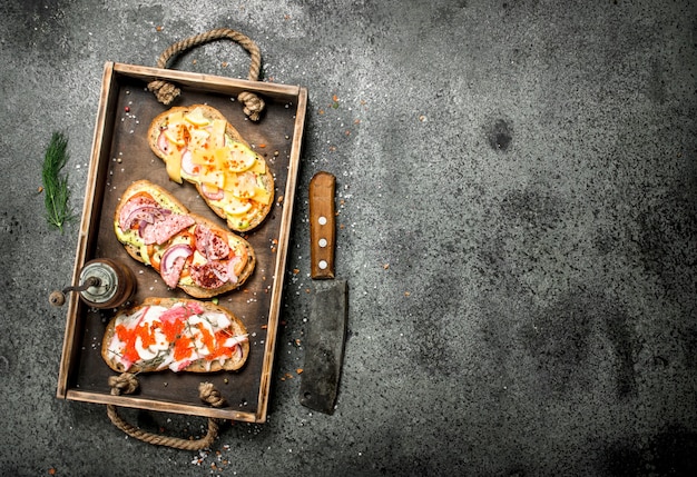 Divers sandwichs aux fruits de mer, viande et légumes sur l'ancien plateau sur table rustique.