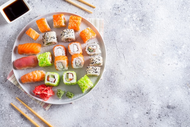 Divers sushis sur plaque avec des bâtons en bois, sauce sur fond de pierre clair