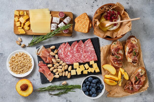 Diverses collations gastronomiques au vin. Bleuets, pêches, craquelins, salami, prosciutto, bruschetta, pistache, pignons de pin, fromages assortis, camembert et fines herbes. Snacks italiens pour des vacances importantes.