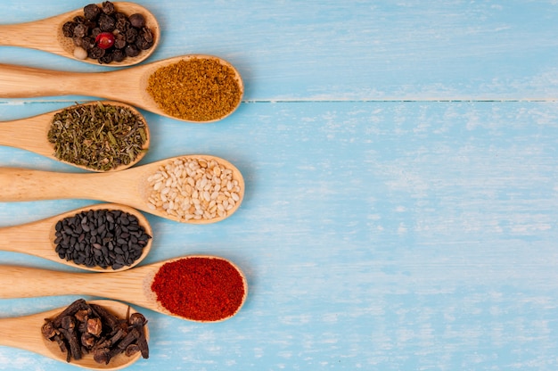 Diverses épices sur cuillères en bois. Ingrédients alimentaires. Table en bois rustique bleu