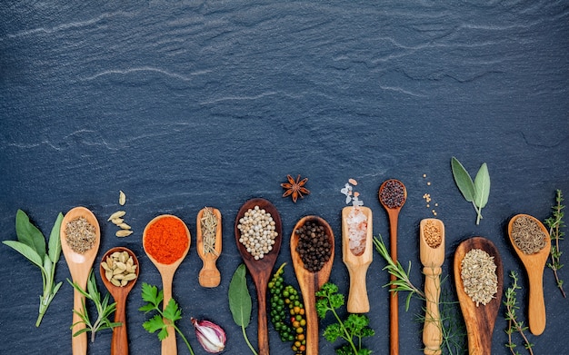 Diverses épices et herbes dans des cuillères de bois sur la pierre noire.