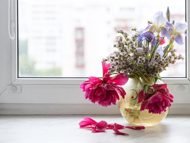 Diverses fleurs dans un vase en verre sur le rebord de la fenêtre