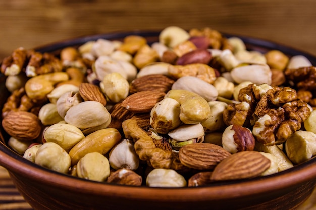 Diverses noix (amande, noix de cajou, noisette, pistache, noix) dans une assiette en céramique sur une table en bois. Repas végétarien. Concept d'alimentation saine