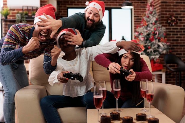 Diverses personnes jouant à des jeux vidéo à la fête de noël, célébrant la fête des vacances d'hiver avec des collègues sur un lieu de travail décoré d'ornements saisonniers. S'amuser à jouer lors d'un événement.