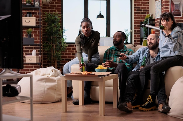 Diverses personnes se rassemblent pour regarder un film ou un film en mangeant du pop-corn, en buvant de la bière et en regardant une émission de téléréalité à la télévision. Groupe d'amis appréciant le contenu du cinéma avec des collations et des boissons.