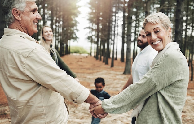 Diversité tenant la main et la famille lors d'une promenade dans la nature en forêt pour créer des liens entre le bien-être ou des vacances saines en plein air Portrait de grands-parents âgés âgés pour les soins d'amour interracial et la confiance dans une aventure amusante