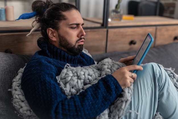 Divertissement moderne. Homme triste et triste utilisant sa tablette tout en essayant de se divertir