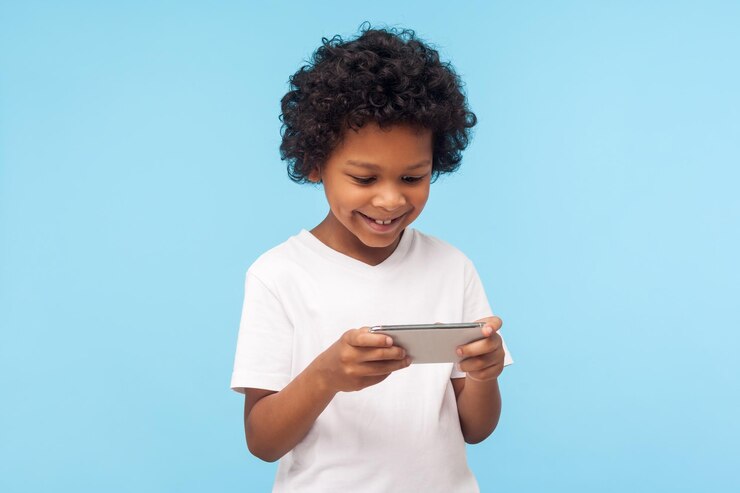 Photo divertissement et technologie pour enfants. joyeux petit garçon excité et mignon aux cheveux bouclés à l'aide d'un téléphone portable et d'un enfant souriant et heureux jouant à un jeu vidéo sur un téléphone portable, bavardant sur un réseau social. intérieur