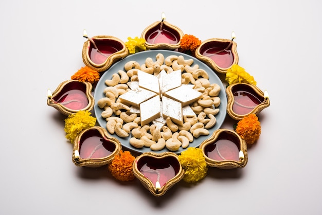 Diwali food Rangoli utilisant Kaju Katli sweet avec Clay diya ou lampe et fleurs de souci disposées en motif circulaire, mise au point sélective