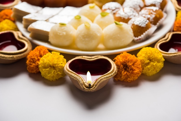 Diwali Rangoli fait à l'aide de Diya ou d'une lampe à huile, de fleurs et d'une assiette pleine de Gulab Jamun, Rasgulla, kaju katli, morichoor ou Bundi Laddu, Gujiya ou Karanji