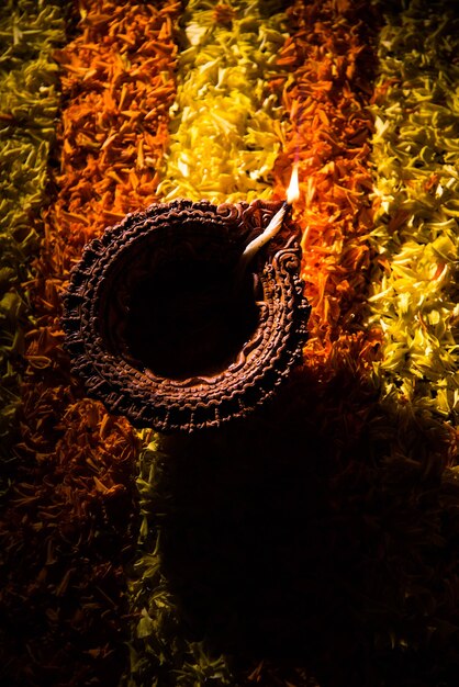 Diya ou lampe à huile traditionnelle allumée sur rangoli coloré composé de pétales de fleurs, sur le festival des lumières appelé diwali ou deepawali, mise au point sélective