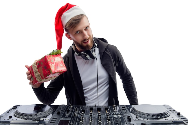 Un dj amusant dans une boîte-cadeau secouant le chapeau du père Noël tout en se tenant derrière une fête du nouvel an au plateau tournant