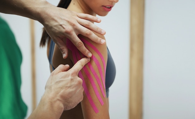 Le docteur aide la femme par le traitement de l'épaule avec du ruban kinesio.